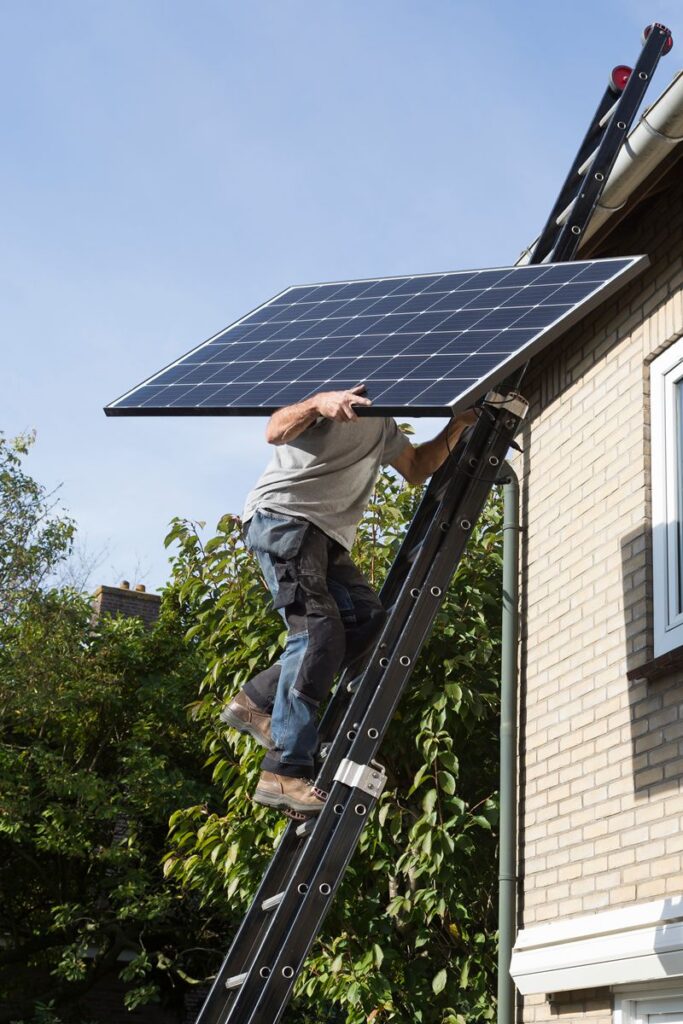 Man carrying a solar panel to a roof using a ladder